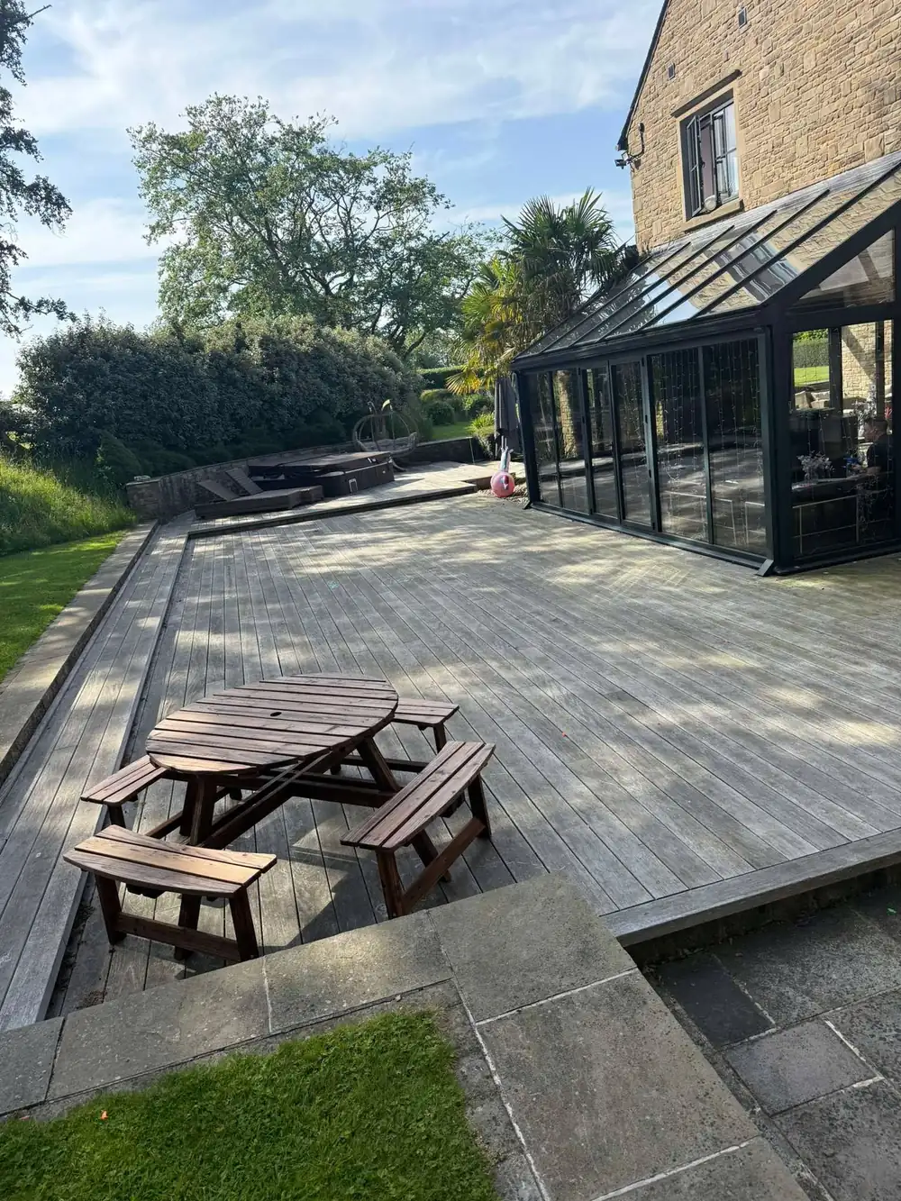 Grey, weathered decking beside a conservatory before cleaning