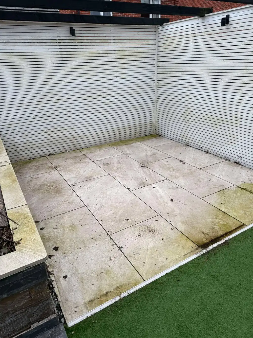 Dirty, algae-stained light porcelain patio before cleaning