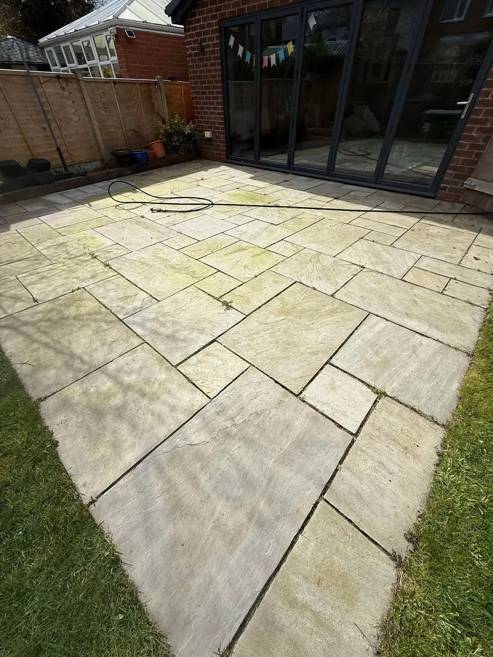 Green, dirty Indian sandstone garden patio before cleaning